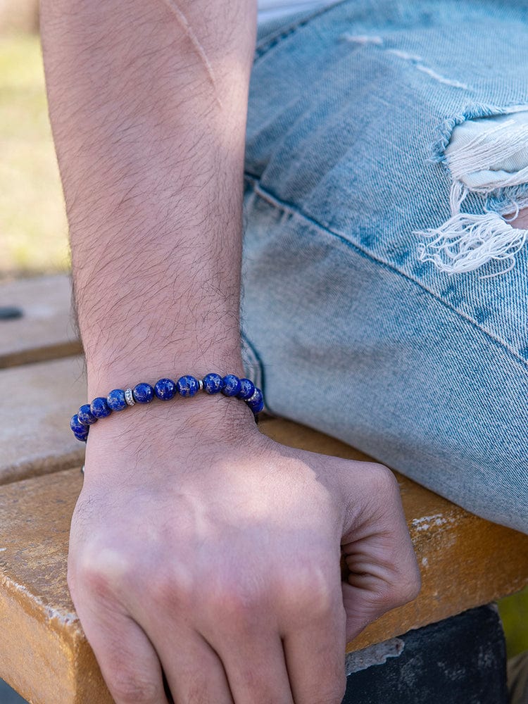 Close-up of a man wearing a men's lapis lazuli beaded bracelet on his wrist, paired with distressed blue jeans.