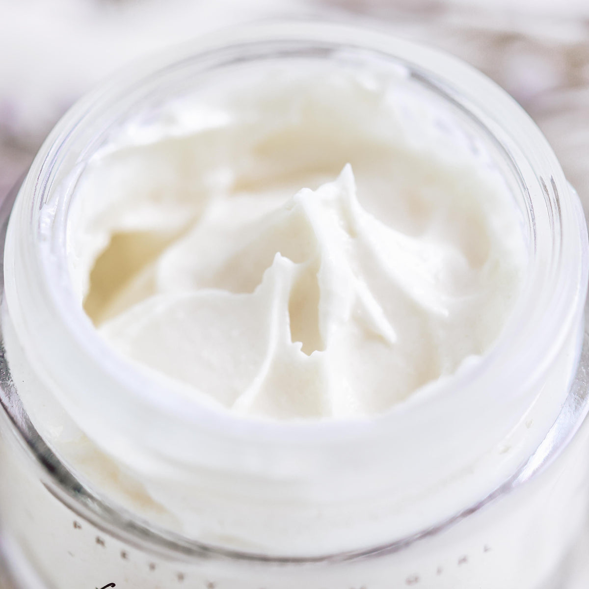 Close-up of Fresh Face Cream Anti-Aging Tallow Moisturizer in a clear glass jar with a smooth, creamy texture.