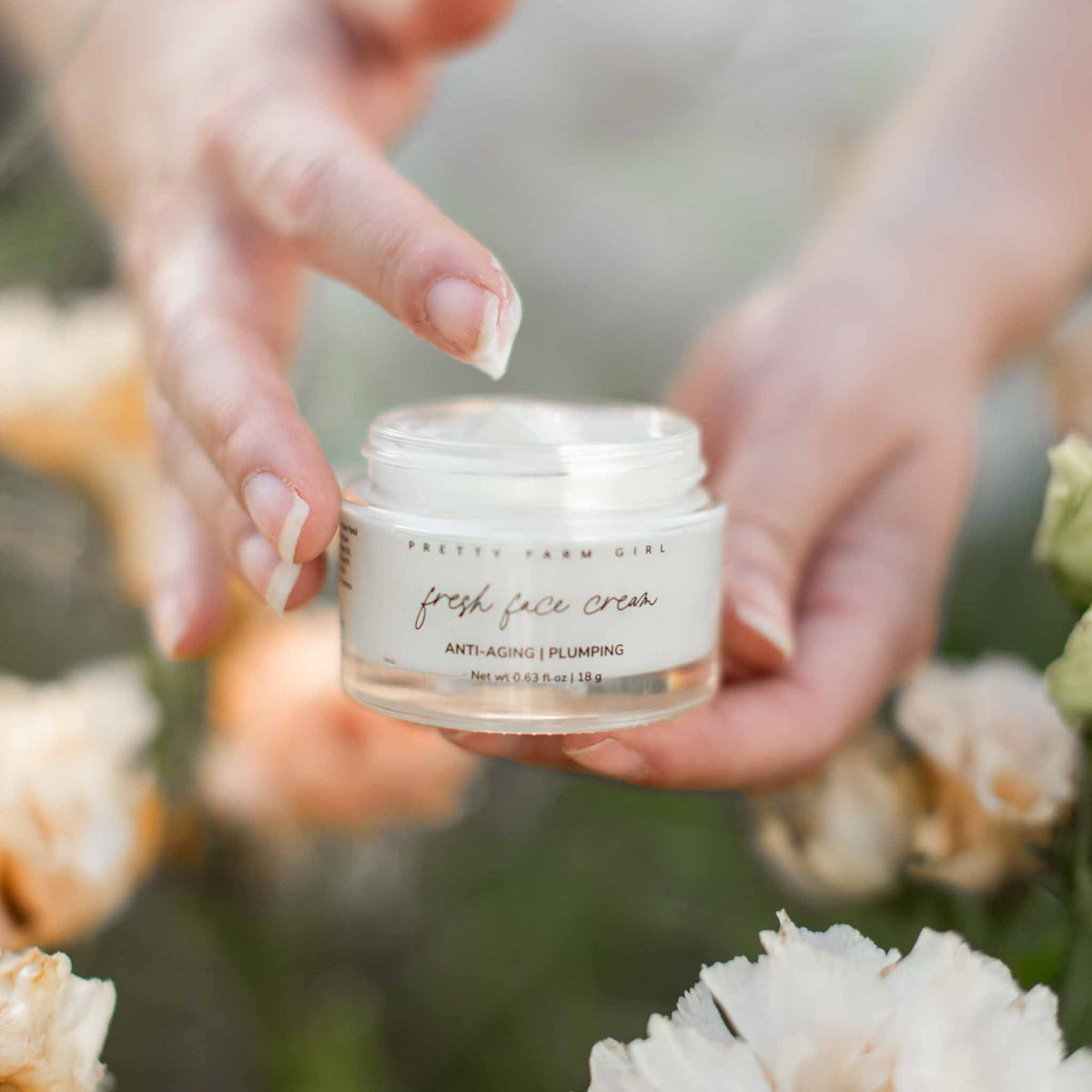 Fresh Face Cream Anti-Aging Tallow Moisturizer in glass jar held by hand among flowers.