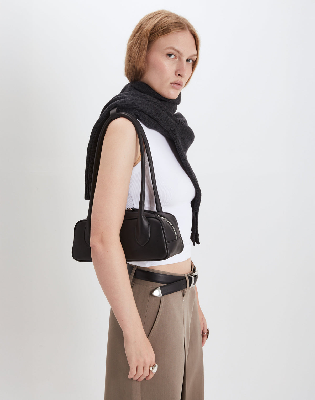 Woman holding a structured leather baguette bag, styled with a black scarf and neutral outfit, showcasing modern fashion.