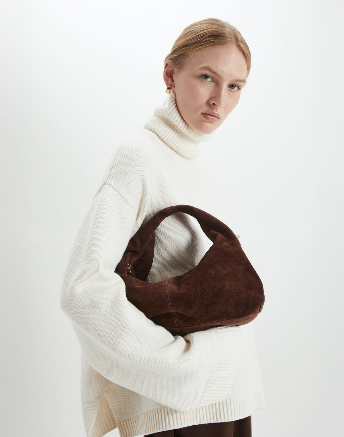 Model wearing a cozy sweater while holding a mini everyday shoulder bag in rich chocolate brown suede.