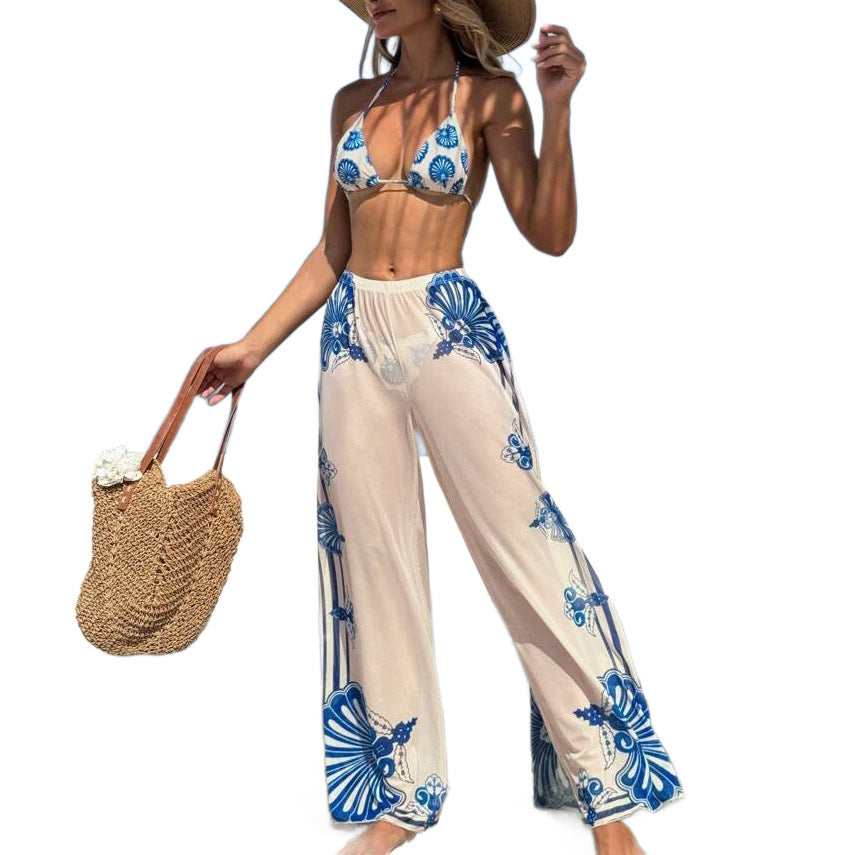 Woman wearing a floral print bikini with tie straps and beach pants, holding a straw bag.
