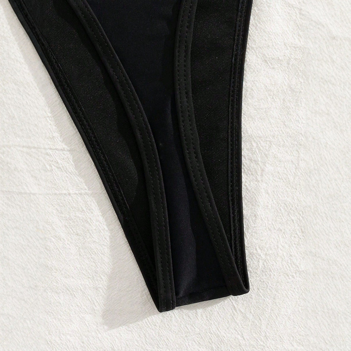 Close-up of black halter bikini set, showcasing high-cut edges and sleek design on a smooth surface.