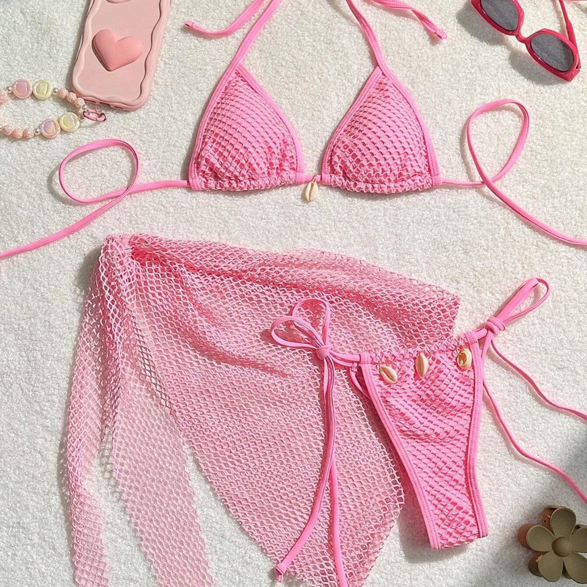 Three piece bikini swimsuit for women in pink color with a stylish design and mesh fabric laying on a white background.
