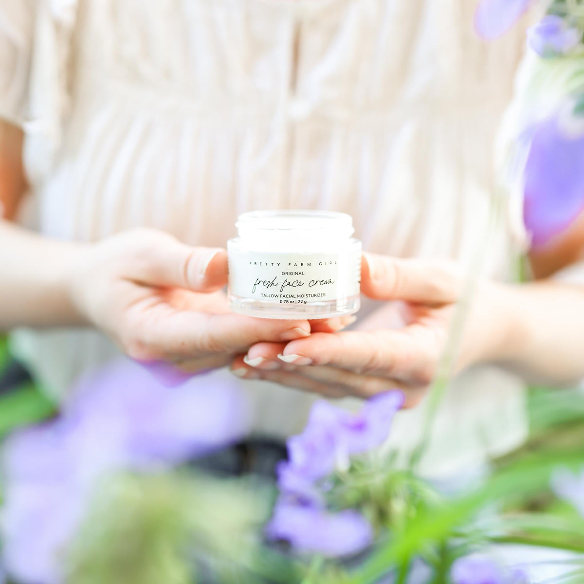Fresh Face Cream anti-aging tallow moisturizer in a glass jar held among purple flowers.
