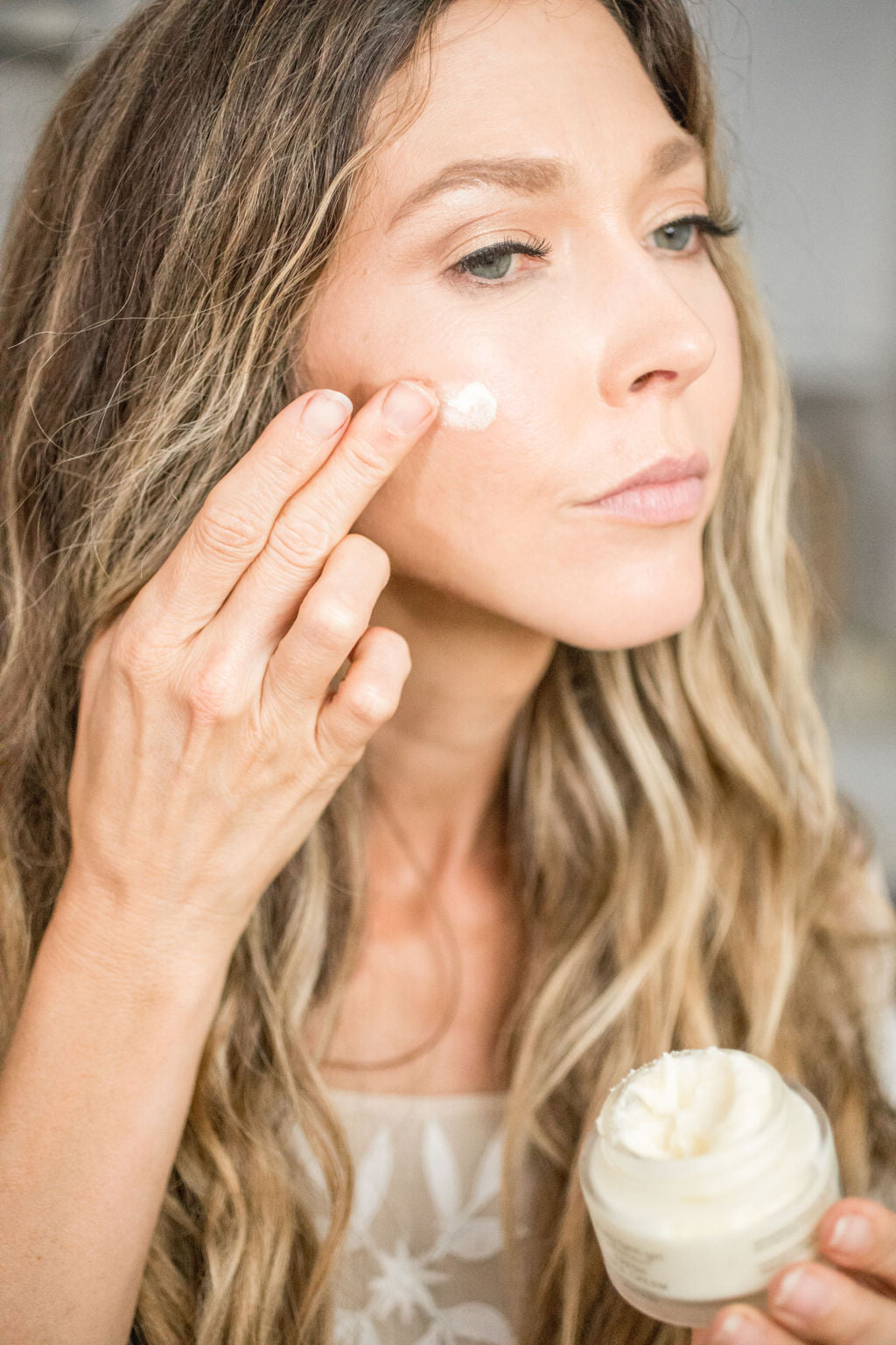 Woman applying Fresh Face Cream Anti-Aging Tallow Moisturizer to her face in a glass jar.