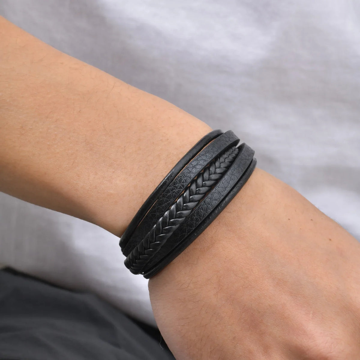 Close-up of a mens braided leather bracelet on a wrist, showing the multi-layer black PU leather design.