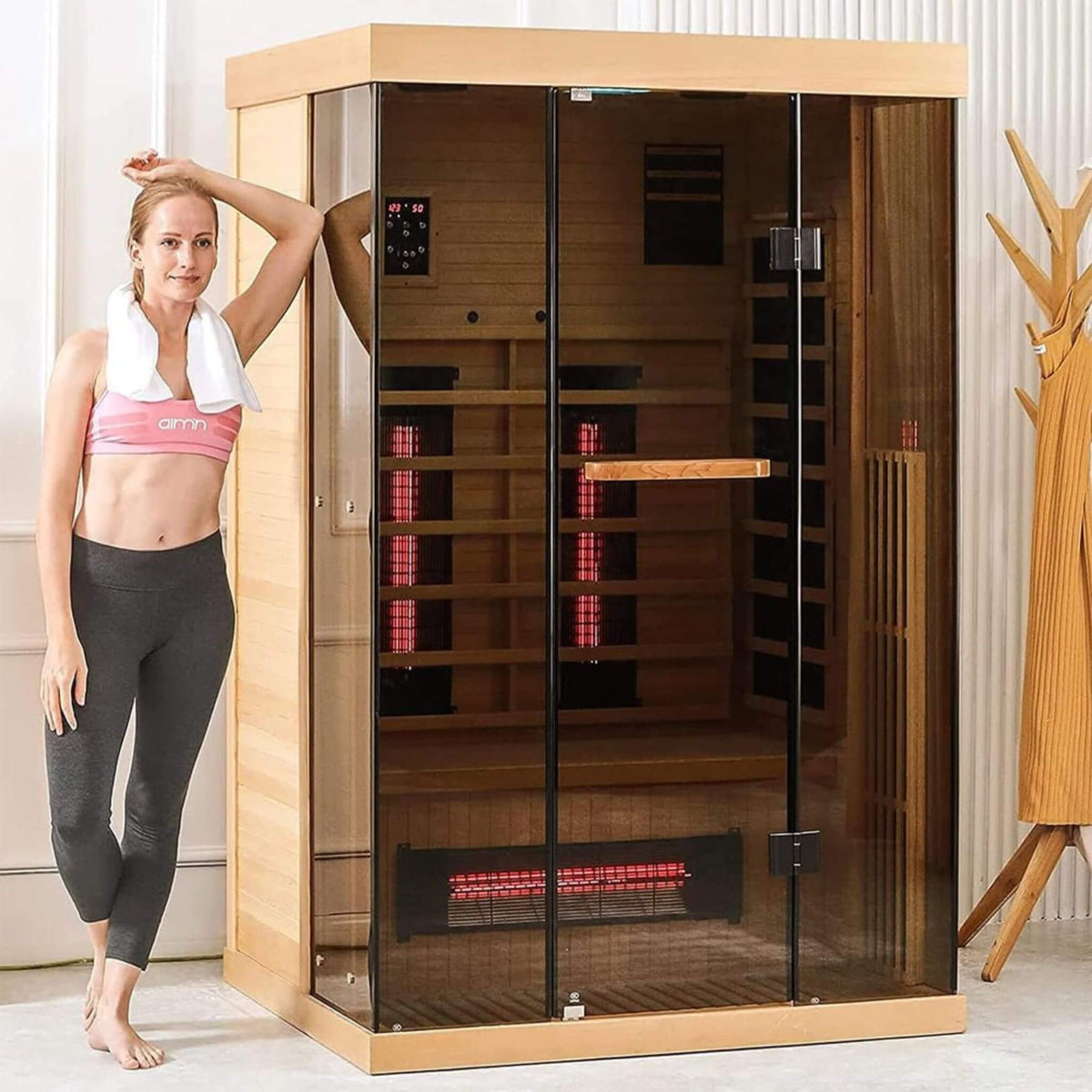 Woman relaxing beside a Valen Luxury low EMF infrared sauna for two with panoramic tempered glass.