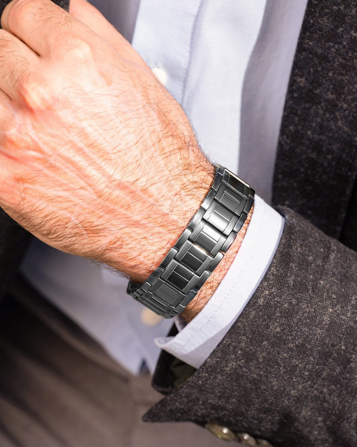 Gunmetal titanium magnetic bracelet for men worn on a wrist, styled with a grey blazer and dress shirt.