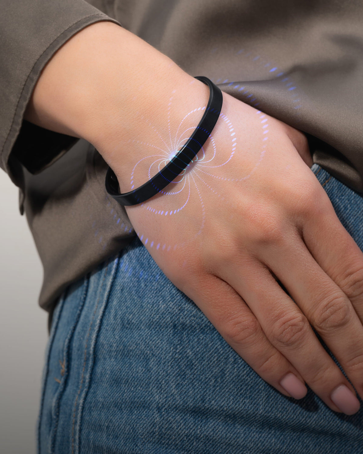A brushed black mens magnetic cuff bracelet on a wrist with a glowing blue magnetic field energy graphic.