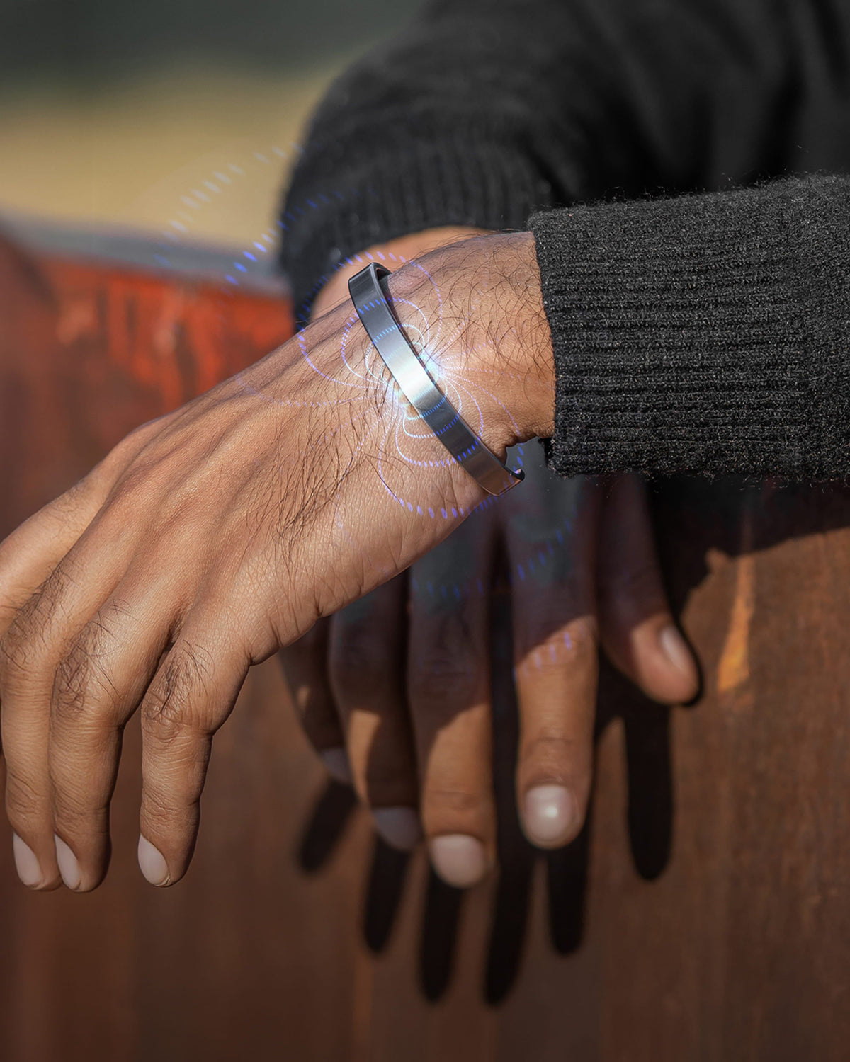 A brushed silver mens magnetic cuff bracelet on a man's wrist with a visual representation of magnetic therapy energy waves.